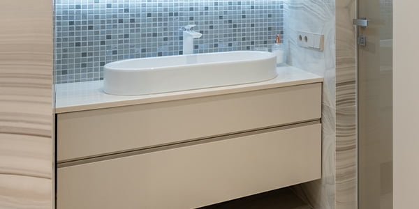 accessibility-in-the-toilet-room bathroom vanity in hotel toilet room with tan walls and cabinets, blue backsplash, white sink basin and silver faucet.