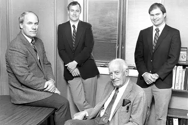 1980-ownership-transition-600×400 four lensing owners in 1980 wearing suits and posing for photo inside office