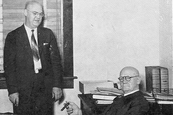 antique photo of two older white men in suits inside business office
